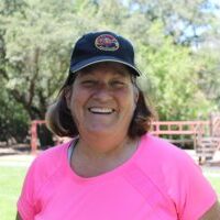 A woman in pink shirt and hat standing next to trees.