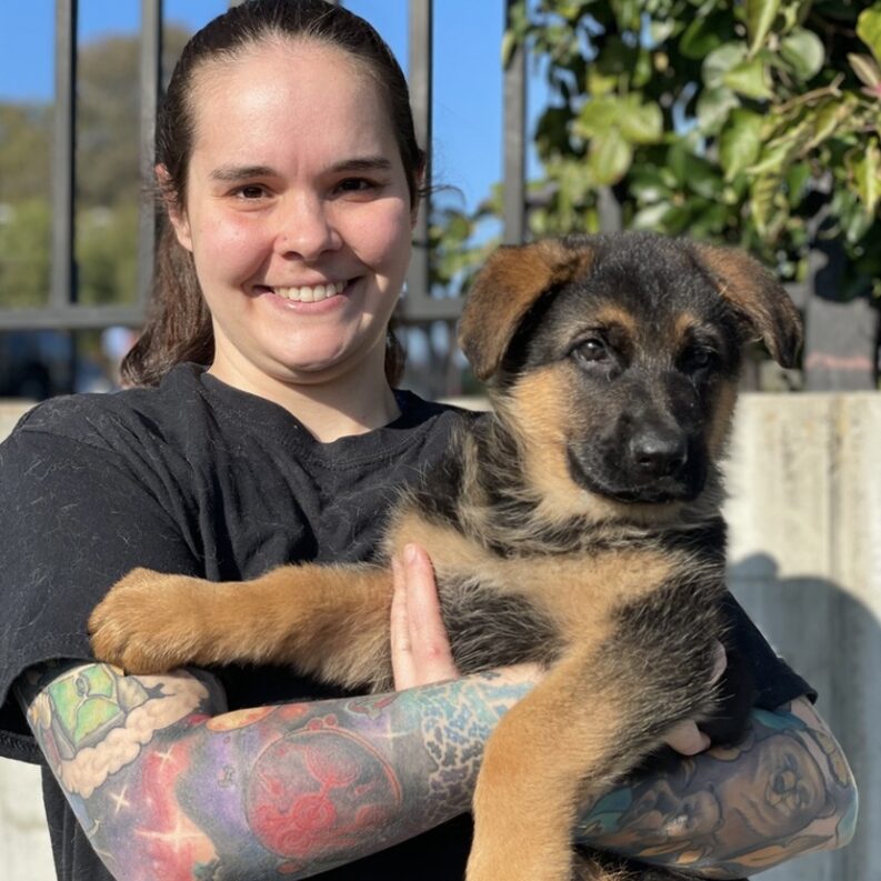 A woman holding a dog with tattoos on her arm.